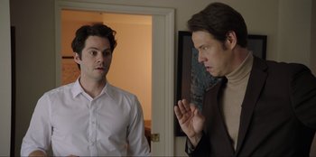 Movie still from “Maximum Truth” (2023), directed by David Stassen – Two men standing next to each other in front of a door; Medium shot, Over the shoulder angle