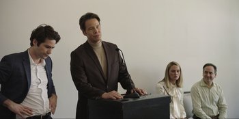 Movie still from “Maximum Truth” (2023), directed by David Stassen – A man standing at a podium speaking to a crowd; Medium shot, Over the shoulder angle