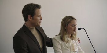 Movie still from “Maximum Truth” (2023), directed by David Stassen – A man standing next to a woman in front of a microphone; Medium shot, Low angle