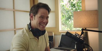 Movie still from “Maximum Truth” (2023), directed by David Stassen – A man with headphones sitting in front of an open laptop computer; Close Up shot, Over the shoulder angle