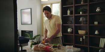 Movie still from “Maximum Truth” (2023), directed by David Stassen – A man standing at a counter cutting vegetables; Medium shot, Over the shoulder angle
