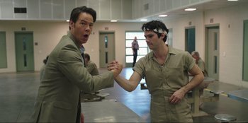 Movie still from “Maximum Truth” (2023), directed by David Stassen – Two men are shaking hands in an empty room; Medium shot, Low angle