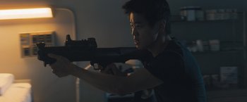 Movie still from “Maze Runner: The Scorch Trials” (2015), directed by Wes Ball – A man holding a gun in a dark room; Medium shot, Low angle