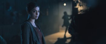 Movie still from “Maze Runner: The Scorch Trials” (2015), directed by Wes Ball – A woman standing in a dark room in front of a group of people; Close Up shot, Over the shoulder angle