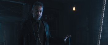 Movie still from “Maze Runner: The Scorch Trials” (2015), directed by Wes Ball – A man standing in a dark room with a microphone; Medium shot, Low angle