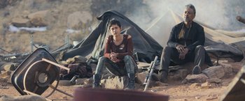 Movie still from “Maze Runner: The Scorch Trials” (2015), directed by Wes Ball – A person sitting on the ground in front of a tarp; Medium shot, Over the shoulder angle