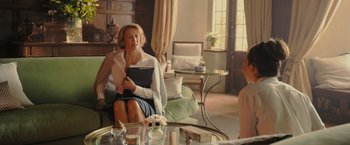 Movie still from “Me Before You” (2016), directed by Thea Sharrock – A woman sitting on top of a couch in a living room; Medium shot, Over the shoulder angle