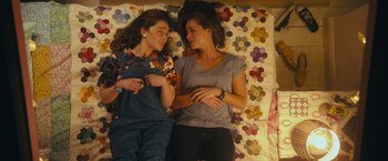 Movie still from “Me Before You” (2016), directed by Thea Sharrock – Two young women laying in a bed with a quilt; Medium shot, Overhead angle