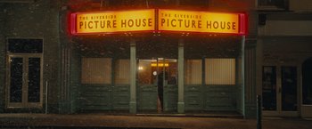 Movie still from “Me Before You” (2016), directed by Thea Sharrock – A person walking in front of a picture house; Extreme Wide shot, Low angle