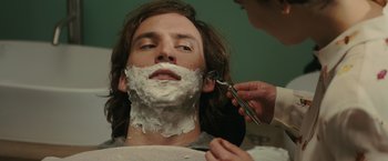 Movie still from “Me Before You” (2016), directed by Thea Sharrock – A man getting his face shaven by a person holding a pair of shears; Close Up shot, Over the shoulder angle