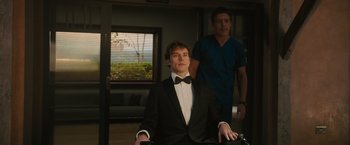 Movie still from “Me Before You” (2016), directed by Thea Sharrock – A man in a suit and bow tie in front of another man; Medium shot, Over the shoulder angle