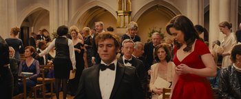 Movie still from “Me Before You” (2016), directed by Thea Sharrock – A man in a tuxedo standing in front of a group of people; Medium shot, Over the shoulder angle