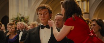 Movie still from “Me Before You” (2016), directed by Thea Sharrock – A man in a tuxedo is being fitted by a woman in a red dress; Close Up shot, Over the shoulder angle
