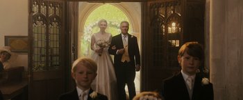 Movie still from “Me Before You” (2016), directed by Thea Sharrock – A man and a woman in wedding attire standing in front of an archway; Medium shot, Low angle