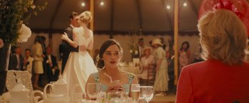 Movie still from “Me Before You” (2016), directed by Thea Sharrock – A woman sitting at a table with a glass in her hand; Medium shot, Over the shoulder angle
