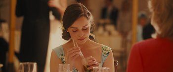 Movie still from “Me Before You” (2016), directed by Thea Sharrock – A woman sitting at a table with a drink in her hand; Close Up shot, Over the shoulder angle