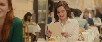 Movie still from “Me Before You” (2016), directed by Thea Sharrock – A woman sitting at a table looking at a piece of paper; Medium shot, Over the shoulder angle