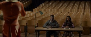 Movie still from “Me Time” (2022), directed by John Hamburg – A man sitting at a table in front of an audience; Wide shot, High angle