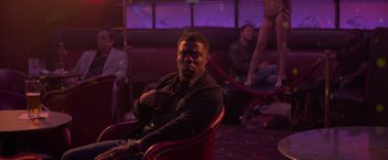 Movie still from “Me Time” (2022), directed by John Hamburg – A man sitting on a chair in a room with other people; Medium shot, Over the shoulder angle