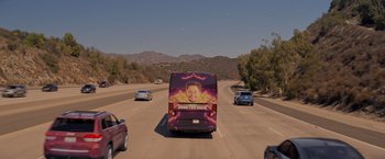 Movie still from “Me Time” (2022), directed by John Hamburg – A bus driving down a street with a picture of a man on it; Extreme Wide shot, High angle