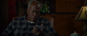 Movie still from “Me Time” (2022), directed by John Hamburg – An older man wearing headphones looking at a cell phone; Close Up shot, High angle
