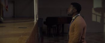 Movie still from “Me Time” (2022), directed by John Hamburg – A man standing in front of a piano in a darkened room; Medium shot, Over the shoulder angle