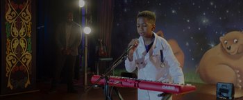 Movie still from “Me Time” (2022), directed by John Hamburg – A young boy in a white lab coat is playing a keyboard; Medium shot, Over the shoulder angle