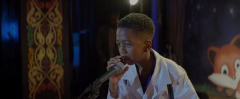 Movie still from “Me Time” (2022), directed by John Hamburg – A boy in a lab coat is holding a microphone; Close Up shot, Over the shoulder angle