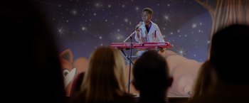 Movie still from “Me Time” (2022), directed by John Hamburg – A young man is standing on a stage with a microphone; Medium shot, Over the shoulder angle