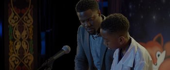 Movie still from “Me Time” (2022), directed by John Hamburg – A man standing next to a microphone next to a young boy; Close Up shot, Over the shoulder angle