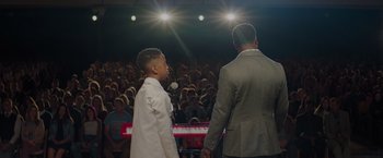 Movie still from “Me Time” (2022), directed by John Hamburg – A man standing next to a young boy on a stage; Medium shot, Over the shoulder angle