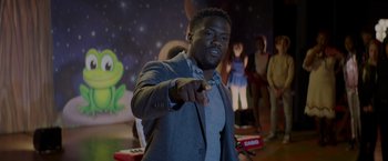 Movie still from “Me Time” (2022), directed by John Hamburg – A man in a gray jacket is holding a remote control; Medium shot, Over the shoulder angle