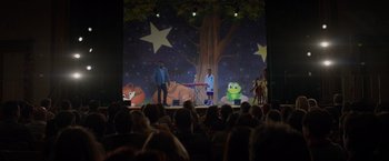 Movie still from “Me Time” (2022), directed by John Hamburg – A group of people on a stage performing a show; Extreme Wide shot, Over the shoulder angle