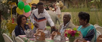 Movie still from “Me Time” (2022), directed by John Hamburg – A man pouring a drink for an older man at an animal themed birthday party; Medium shot, Over the shoulder angle