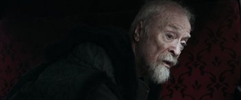 Movie still from “Medieval” (2022), directed by Petr Jákl – An old man with a beard is sitting in a dark room; Close Up shot, Over the shoulder angle