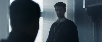 Movie still from “Medieval” (2022), directed by Petr Jákl – A man wearing a crown standing next to a window; Close Up shot, Over the shoulder angle