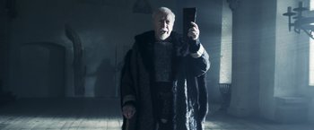 Movie still from “Medieval” (2022), directed by Petr Jákl – An old man in a fur coat holding up a cell phone; Medium shot, Low angle