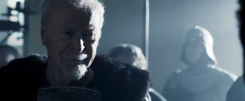 Movie still from “Medieval” (2022), directed by Petr Jákl – An old man with a beard and a fur coat; Close Up shot, Over the shoulder angle