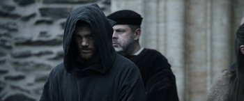 Movie still from “Medieval” (2022), directed by Petr Jákl – A man in a black robe and a man in a black hat; Medium shot, Over the shoulder angle