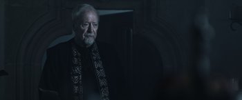 Movie still from “Medieval” (2022), directed by Petr Jákl – An older man with a beard wearing a scarf; Close Up shot, Over the shoulder angle
