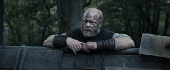 Movie still from “Medieval” (2022), directed by Petr Jákl – An old man with a beard wearing chains; Medium shot, Low angle
