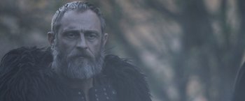 Movie still from “Medieval” (2022), directed by Petr Jákl – A man with a long beard and a black jacket; Close Up shot, Over the shoulder angle
