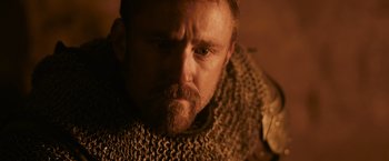 Movie still from “Medieval” (2022), directed by Petr Jákl – A person with a beard wearing chains; Close Up shot, Low angle