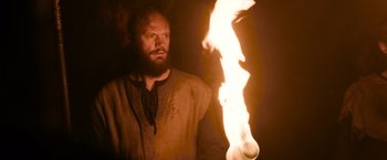 Movie still from “Medieval” (2022), directed by Petr Jákl – A man with a long beard is holding a flame; Medium shot, Low angle