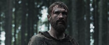Movie still from “Medieval” (2022), directed by Petr Jákl – A man with a beard and face paint in the woods; Close Up shot, Low angle