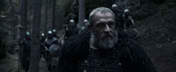 Movie still from “Medieval” (2022), directed by Petr Jákl – A man with a long beard wearing a black outfit; Medium shot, Low angle