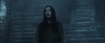 Movie still from “Medieval” (2022), directed by Petr Jákl – A woman standing in the dark in front of a stone wall; Medium shot, Low angle
