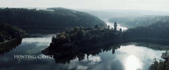Movie still from “Medieval” (2022), directed by Petr Jákl – An aerial view of a lake with a castle on top of it; Extreme Wide shot, High angle