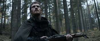 Movie still from “Medieval” (2022), directed by Petr Jákl – A man holding a rifle in the woods; Close Up shot, Low angle