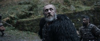 Movie still from “Medieval” (2022), directed by Petr Jákl – An old man with a beard and a black fur coat; Close Up shot, Low angle